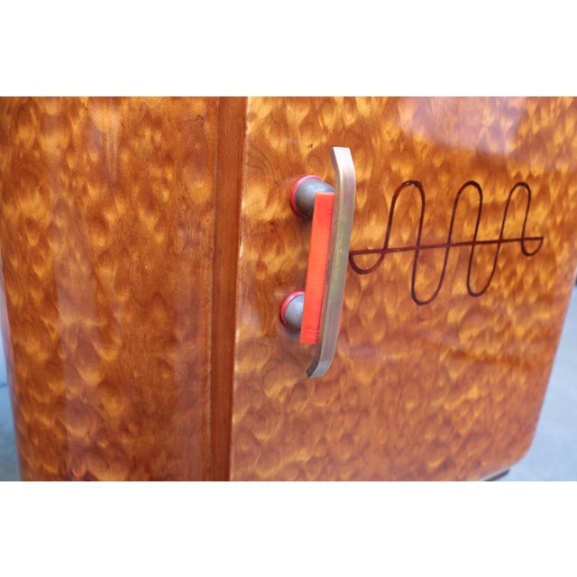 An Art Deco small desk. Amboyna with inlaid details, red bakelite and brass pulls. Desk features four drawers a storage...