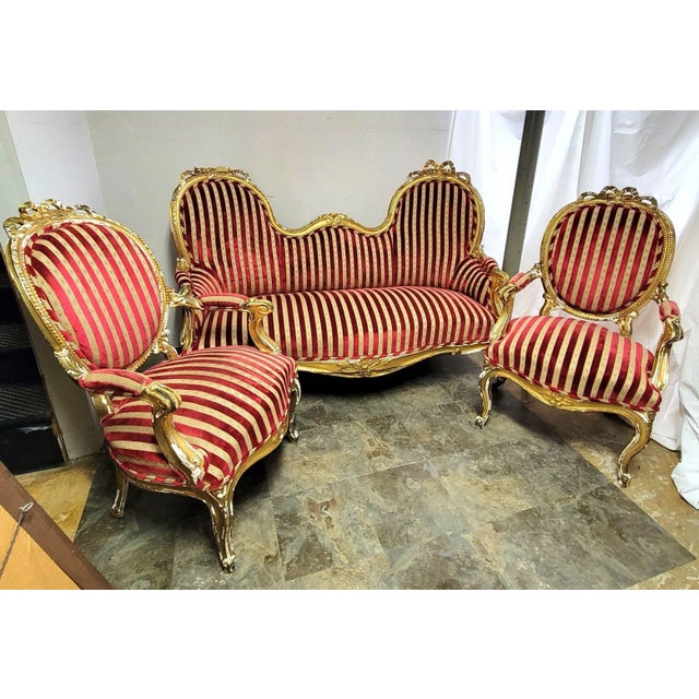 Two fine French hand carved fauteuil chairs and sofa parlor set decorated with a giltwood tied ribbon and bow motif. The...