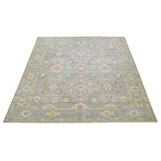 This oversized hand-knotted wool rug features a blue and gray background and a multicolor all-over design. This rug...