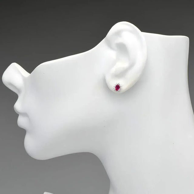 With an oval ruby ringed by a starburst-shaped pattern of miniature diamonds fit in a delicate setting, these studs are...