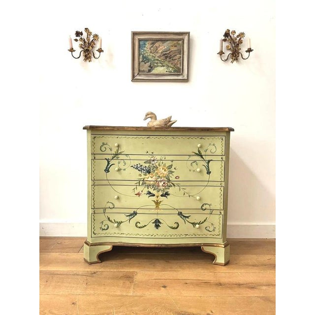 An early 20th-century sage green hand-painted serpentine chest of drawers decorated with floral motifs, scrollwork, and...