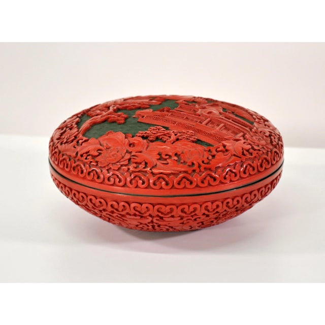 A large vintage Chinese red cinnabar box with deep relief carved lid depicting peonies, trees and a landscape with a...