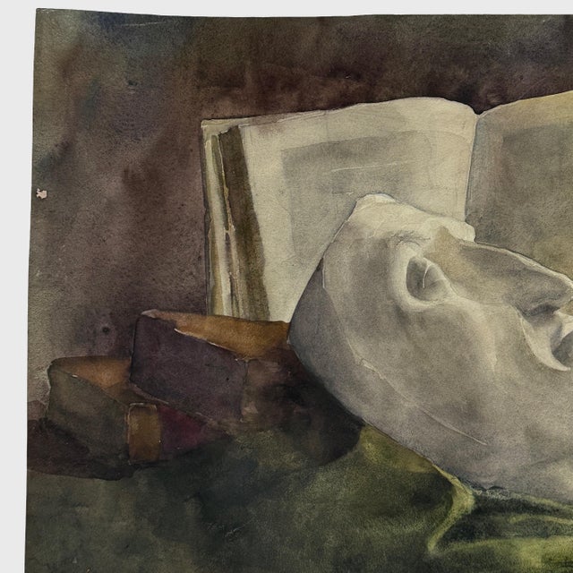 A French still life rendered in watercolor, depicting a death mask supported by two stacked books before an open volume....