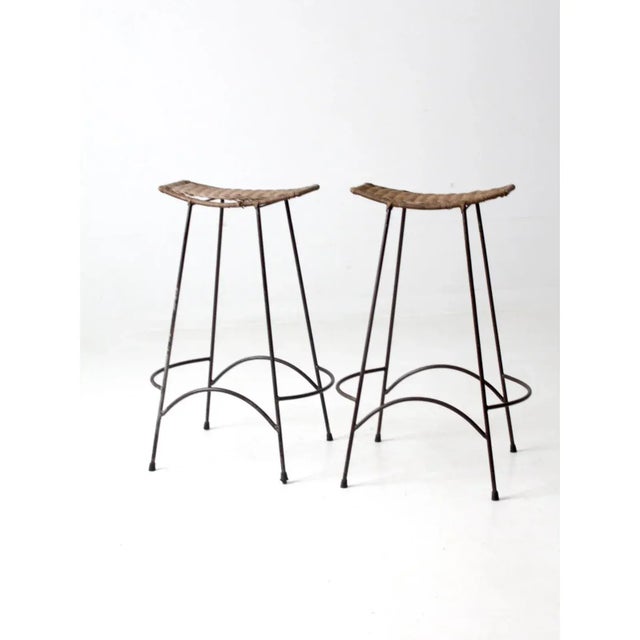 A sleek pair of mid 20th century bar stools featuring iron hairpin legs with distinctive integrated footrests in the...