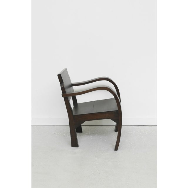 Solid wood 1940s-era armchair with sweeping curved arms, geometric backrest, and dark stained finish. Material Wood...