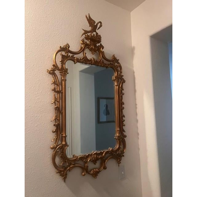 This elegant decorative mirror features an elaborate, ornate gilt frame characteristic of the Rococo or Baroque style. The...