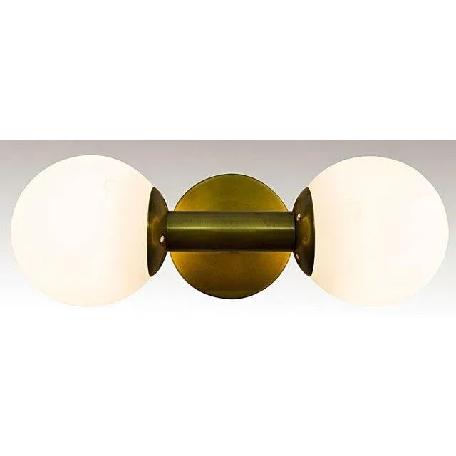 Two white glass orbs concealing 40W bulbs are mirrored by the circle of antique brass that acts as its canopy and suspends...