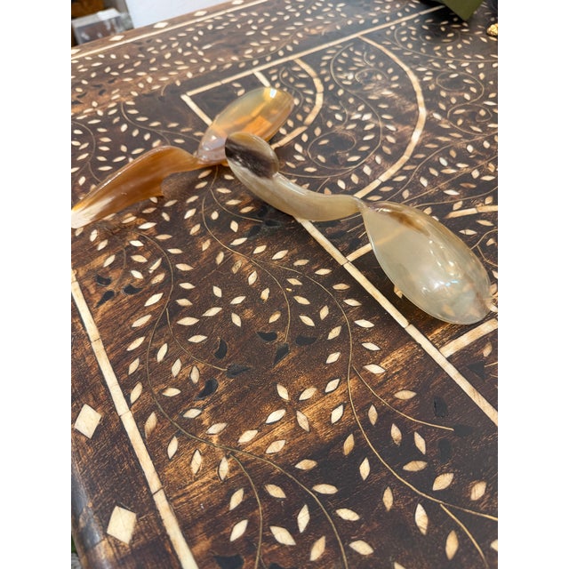 Two hand carved horn decorative spoons. Each spoon handle has a distinctive design and each spoon shows natural varying...