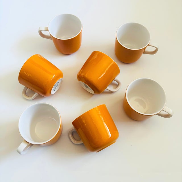 A set of 7 mid century ceramic mugs from the "Pastelle" line by Mikasa. Orange exteriors with white interiors and handles....