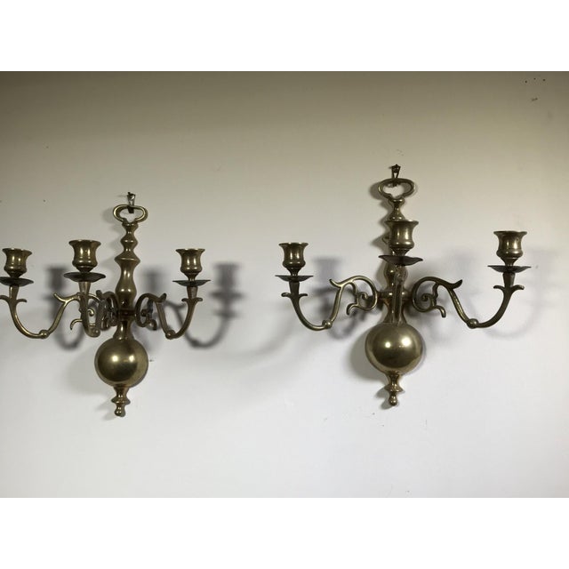 A pair of vintage solid brass three-light wall candle sconces with three curved arms with candle cups, a spherical body...