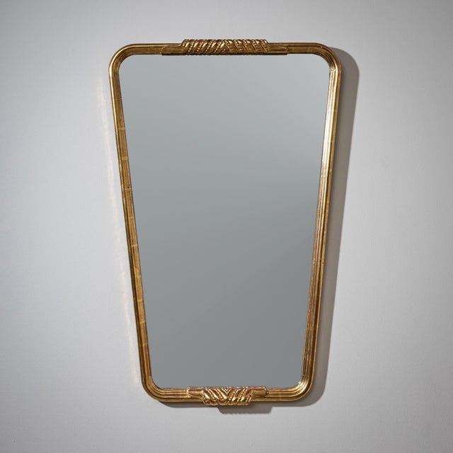 Trapezoidal wall mirror in a molded giltwood frame with shaped accents along the sides. The gilding shows areas of age-...