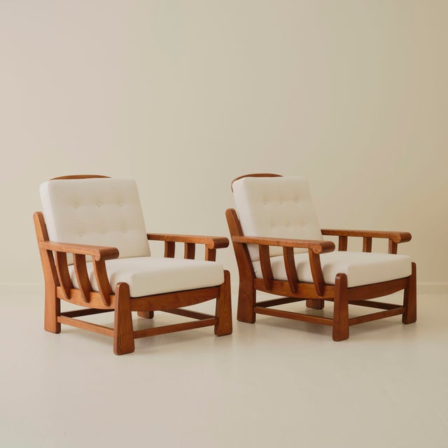 A pair of lounge chairs by Maison Regain, crafted in solid wood with newly upholstered cushions. Each chair is defined by...