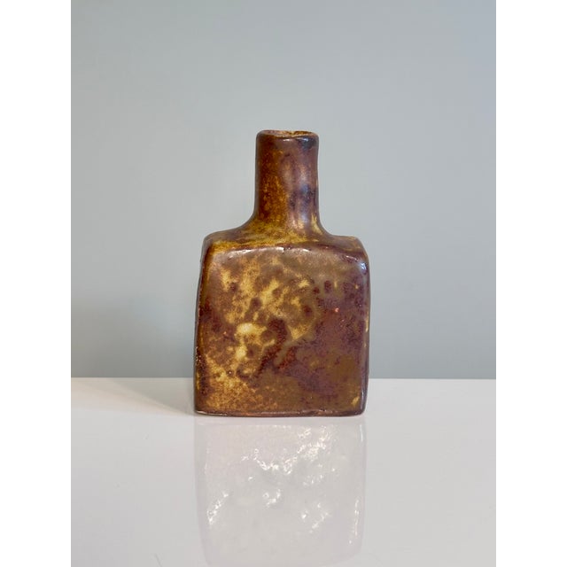 This small, handcrafted, free-form ceramic vase, in warm earth tones and featuring a play of matte and glossy glaze, was...