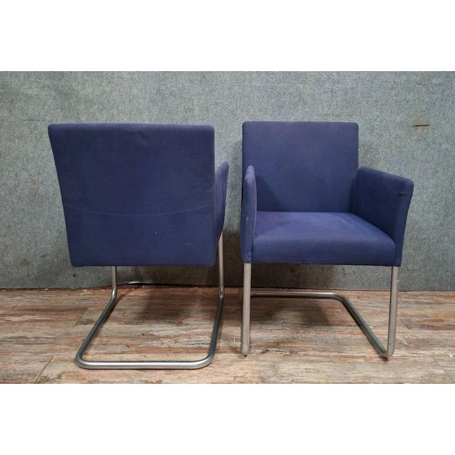 Pair of modern armchairs with clean lines, resting on a chromed tubular metal frame with a sled base. The wide,...