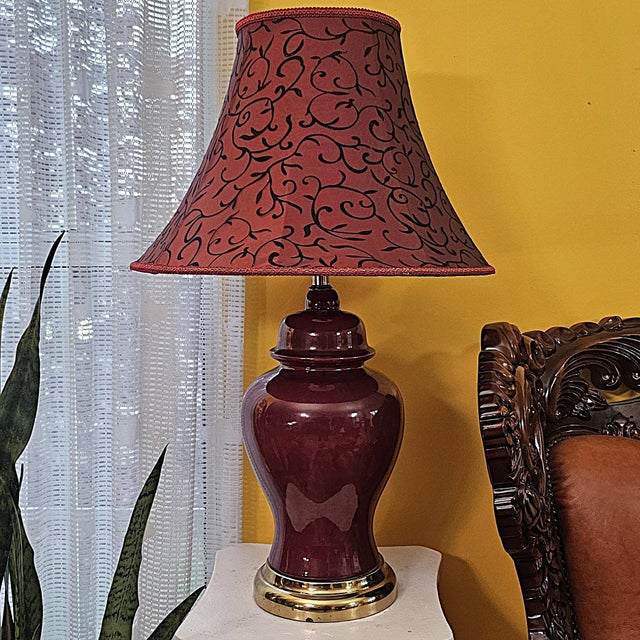 Vintage Chinese flambe porcelain urn lamp featuring a lustrous deep oxblood red glaze, polished brass-tone base, and...