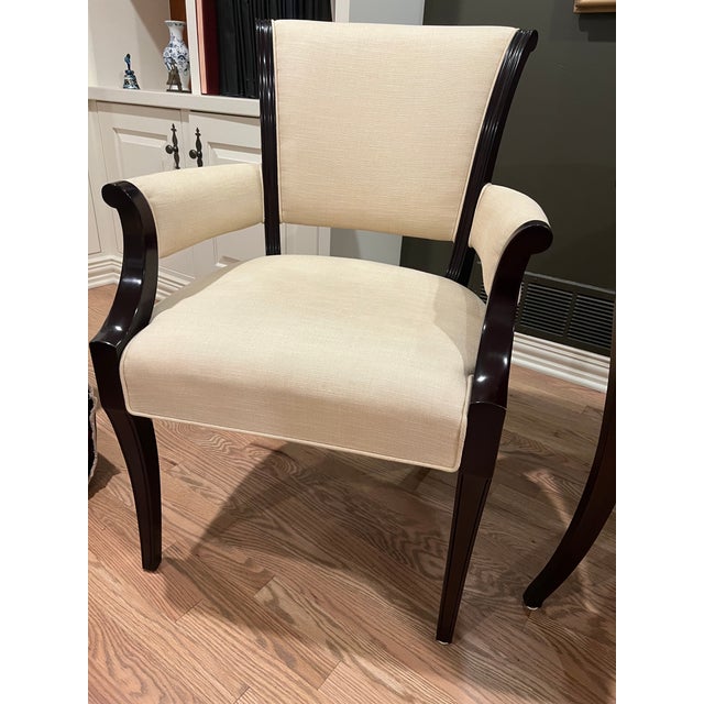 Elegant armchairs with dark-stained wood frames and cream-colored fabric upholstery. The chairs have curved armrests with...