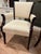 Elegant armchairs with dark-stained wood frames and cream-colored fabric upholstery. The chairs have curved armrests with...