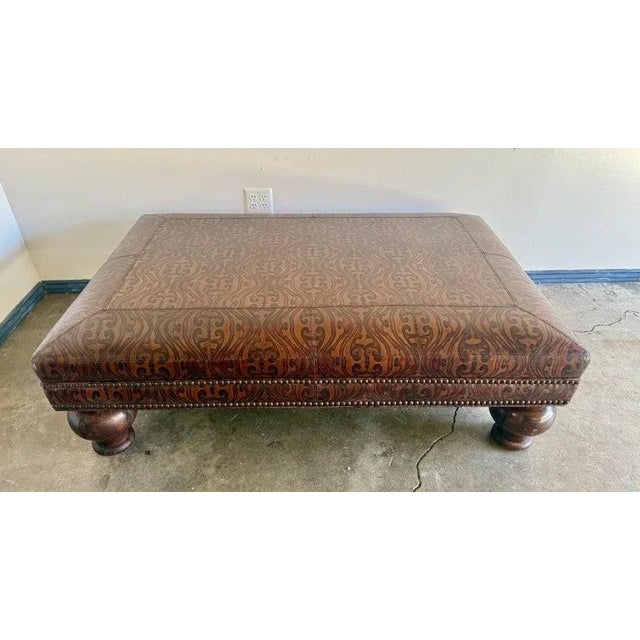 A substantial rectangular ottoman upholstered in richly embossed leather, mid-20th century. The warm brown leather...