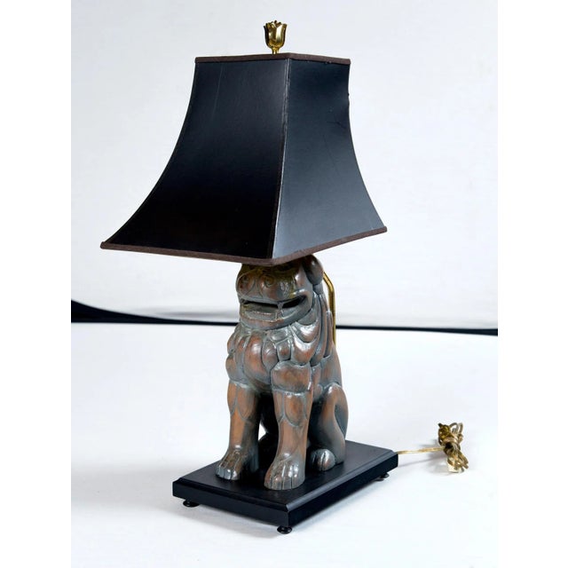 A pair of carved wood Foo Dog lamps by Sarreid of Spain. Shaped black paper lamp shades with gold interiors. Dogs are...