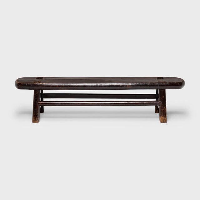 A low daybed step from the mid-19th century, featuring an elongated plank top with rounded ends and short splayed legs...