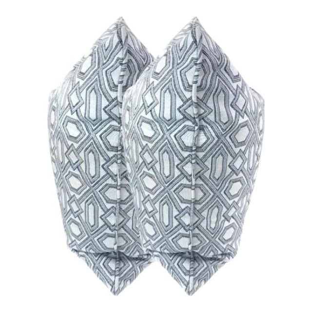 The pillows are a geometric pattern with a soft, neutral palette — primarily light gray/blue and white tones. The design...