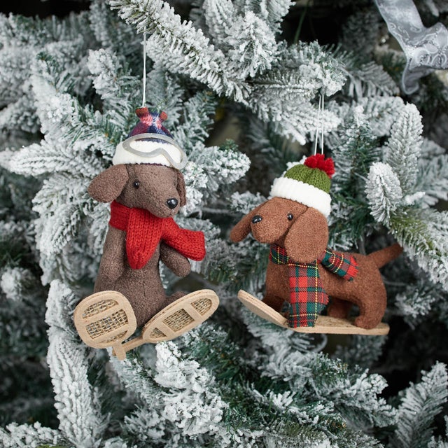 Bring playful charm to your holiday decor with these Plush Ski and Snowboard Dog Ornaments. Featuring festive red and...