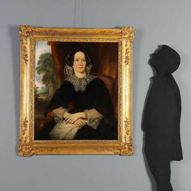 Oil on canvas. 19th-century English school. Half-length portrait of a lady seated at a window overlooking a landscape of...