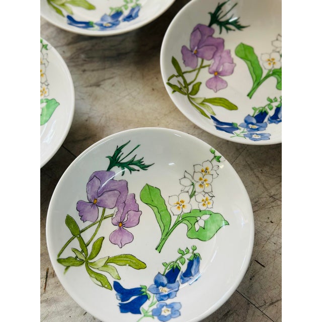 A charming set of four hand-painted porcelain bowls featuring delicate botanical illustrations in soft watercolor tones....