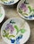 A charming set of four hand-painted porcelain bowls featuring delicate botanical illustrations in soft watercolor tones....