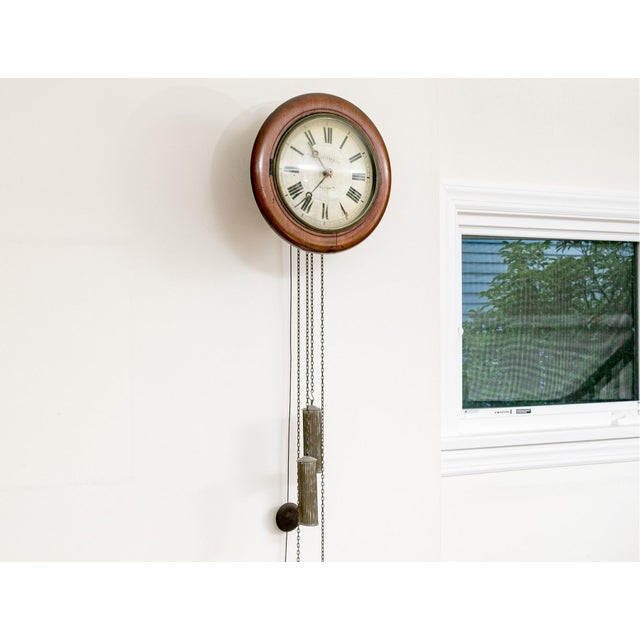 An antique wall mounted clock with a round mahogany case, Roman numeral enamel dial, brass hands and two weighted, chain-...