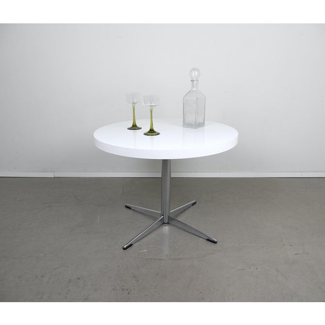 Round side table from the 1970s. The cross base is made of chrome-plated metal. The tabletop is white laminated.