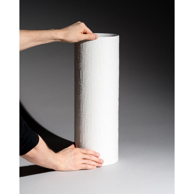 Tall cylindrical floor vase in matte white bisque porcelain with a rhythmic relief of abstract glyph-like motifs. The...