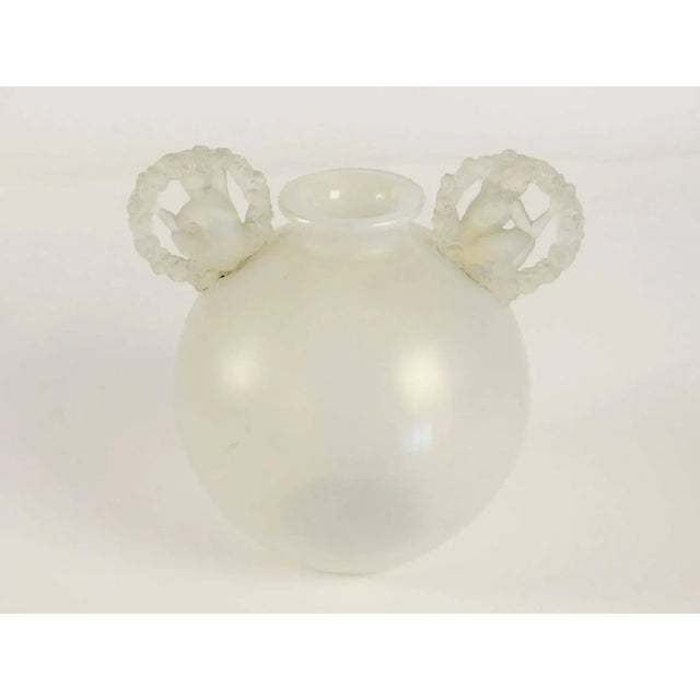 - White opalescent glass container - Attached ears under the rim of a nude female figure inside a circular garland of...