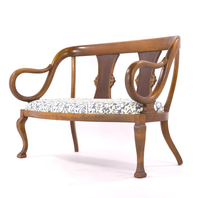 Elegant vintage two-seat settee featuring a sculptural Neoclassical Revival design with dramatic open lyre-form arms, a...