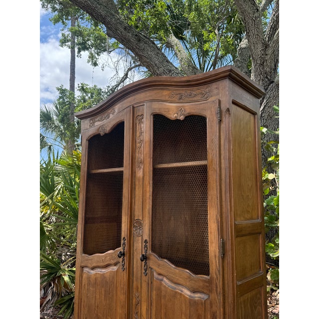 A beautifully detailed vintage French Provincial armoire, showcasing elegant curves, hand-carved motifs, and a warm,...