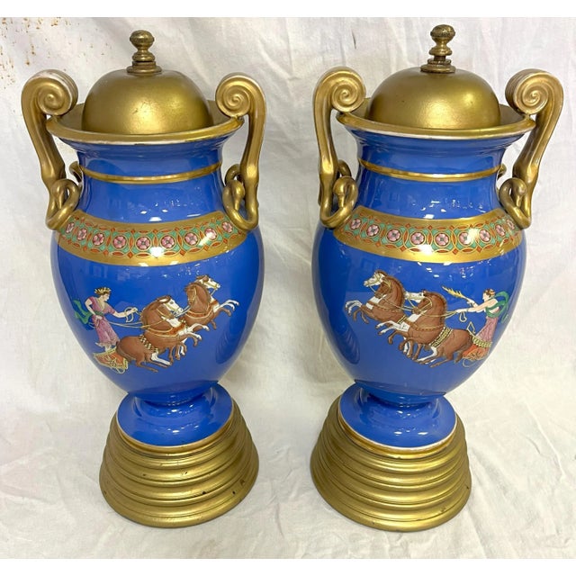 Cool pair of European Neoclassical hand painted porcelain urns from the 1920's. Each has a blue background with different...