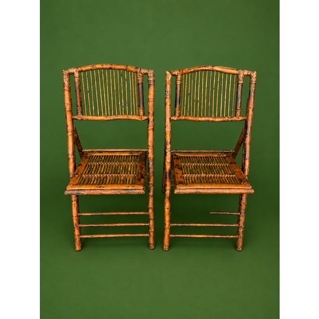 A charming pair of vintage 1950s bamboo folding chairs featuring slender vertical spindle backs, woven/slatted seats and...