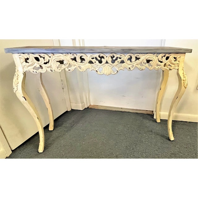 Pretty coastal style carved wood console table. The apron and base have carved scroll details with an ivory color...