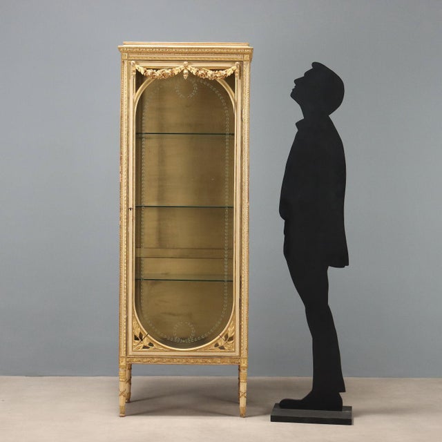 Neoclassical-style display cabinet, carved, lacquered, and gilded. Front door and sides with beveled glass and etched leaf...