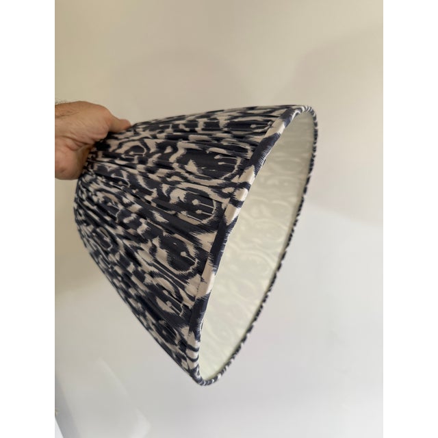 A beautiful fabric-covered lampshade with a pleated design. The fabric features a navy blue and white Ikat-style pattern,...