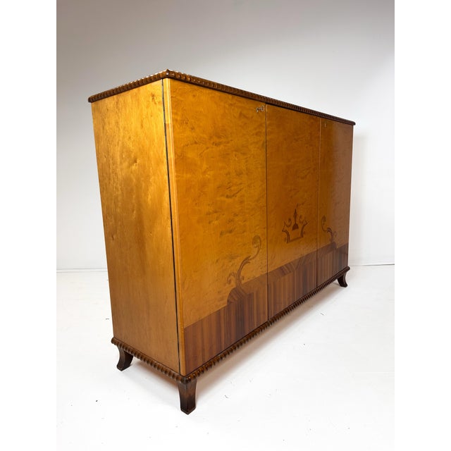 1930's Swedish Grace Cabinet. 3 large doors conceal interior adjustable shelves and small drawers. Mixed woods create...