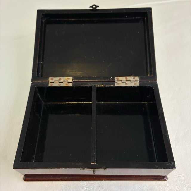 This Japanese lacquerware trinket box displays a rich mahogany-toned finish adorned with a hand-painted floral and...