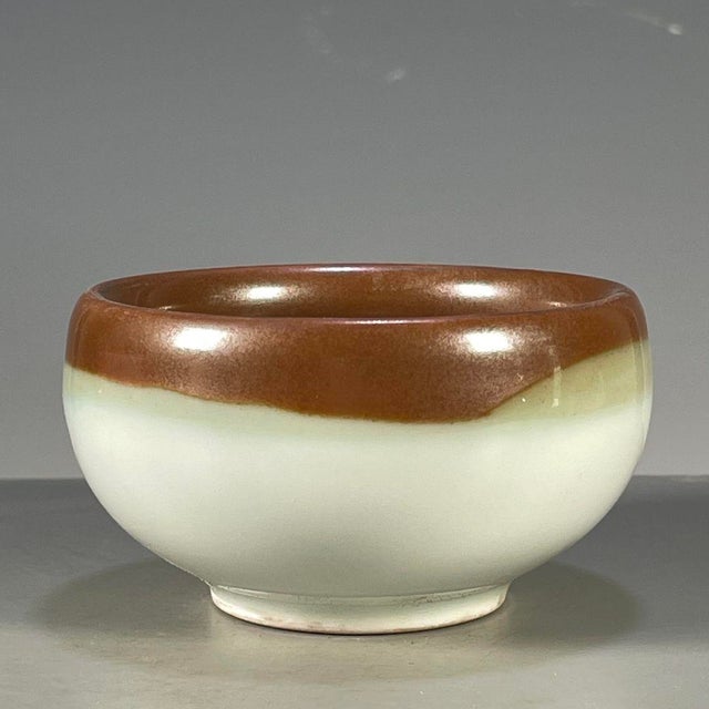 A charming Chinese ceramic tea cup or small bowl. The piece features a striking two-tone glaze, with a rich, glossy brown...
