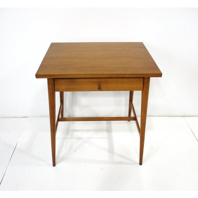 One maple nightstand with a single drawer having a brass pull, conical legs, middle and side to side stretchers. By the...