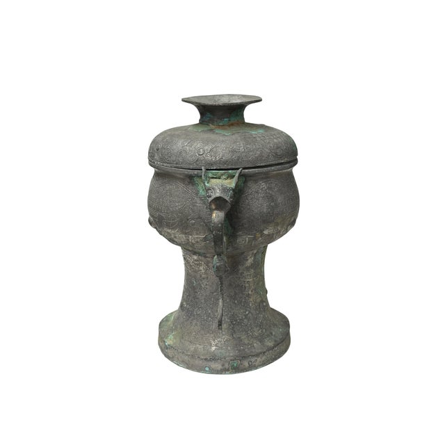 This ornate bronze vessel, an exquisite example of ancient ritual craftsmanship, displays a weathered dark-grey patina...