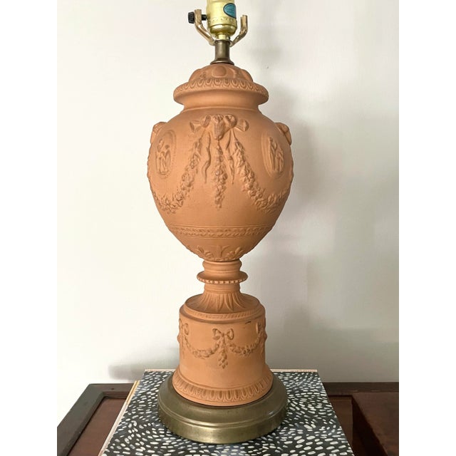 Vintage Neoclassical style terra cotta table lamp featuring raised floral swags, rams’ heads, and figural motifs. Aged...