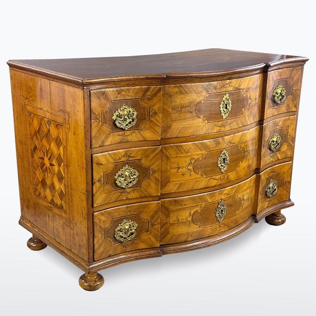 Baroque chest of drawers with serpentine front and rich marquetry decor. Professionally restored, featuring original brass...
