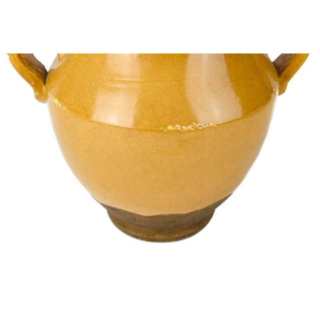 A traditional French earthenware confit jar with a bulbous body and two curled loop handles at the shoulders. The top...