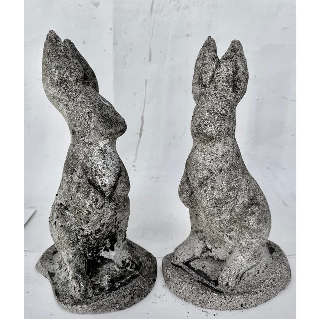 A charming pair of composition stone garden rabbits, each modeled seated upright with alert ears, tucked front paws, and...