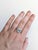 An aquamarine glows in a cool, serene blue at the centre of this solid 14K white gold ring, encircled by sixteen earth-...